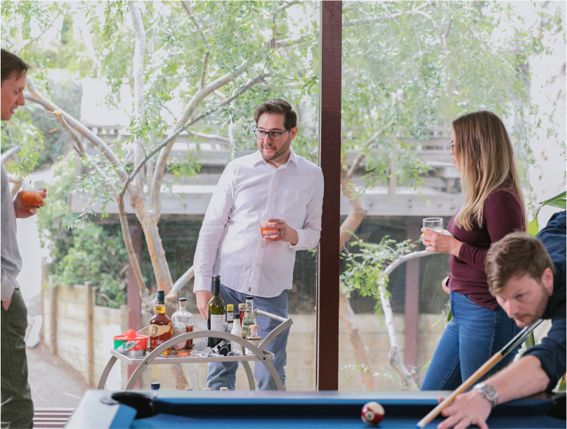 Team members standing around a small bar and pool table drinking and playing pool